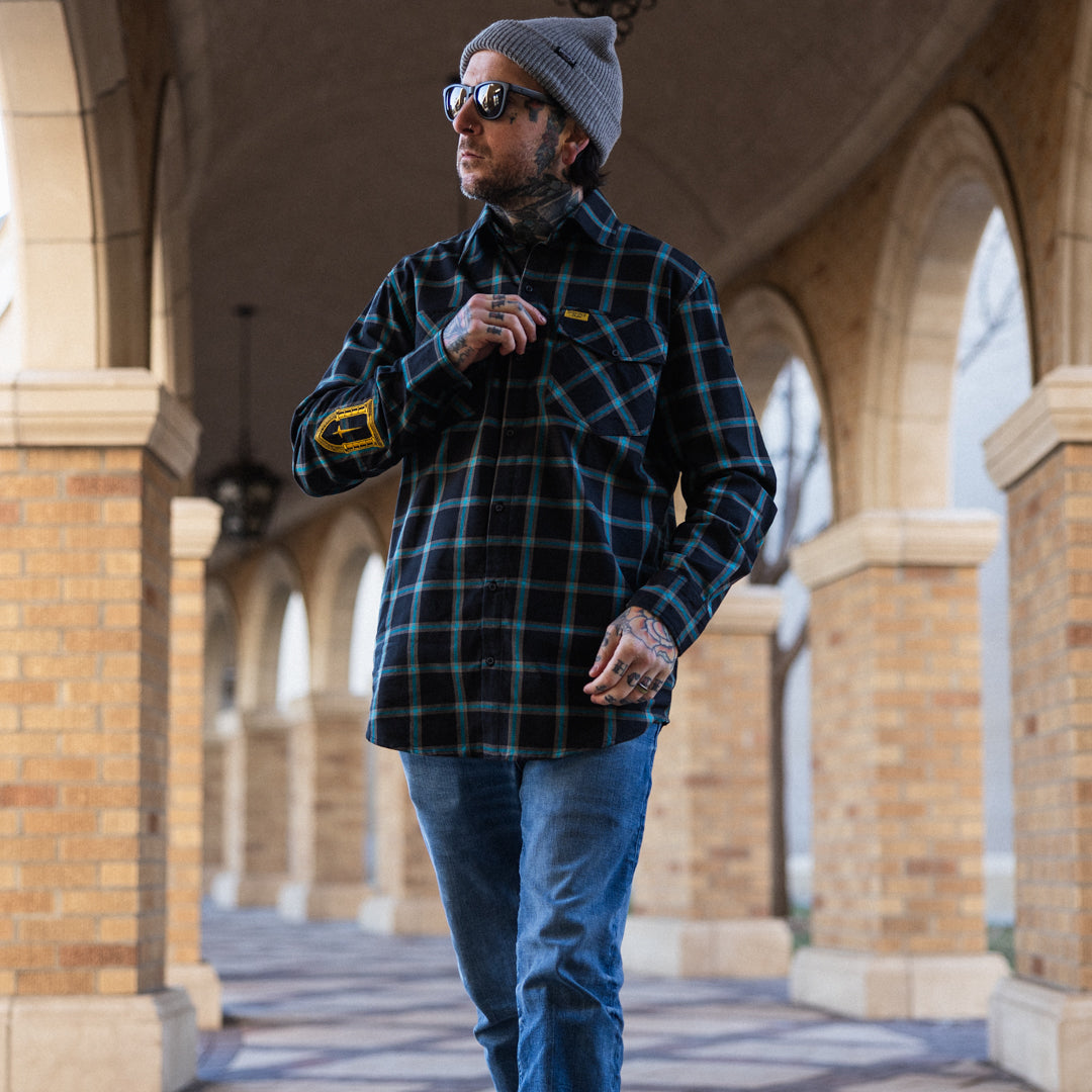 Man wearing a plaid shirt and sunglasses walking through an archway.