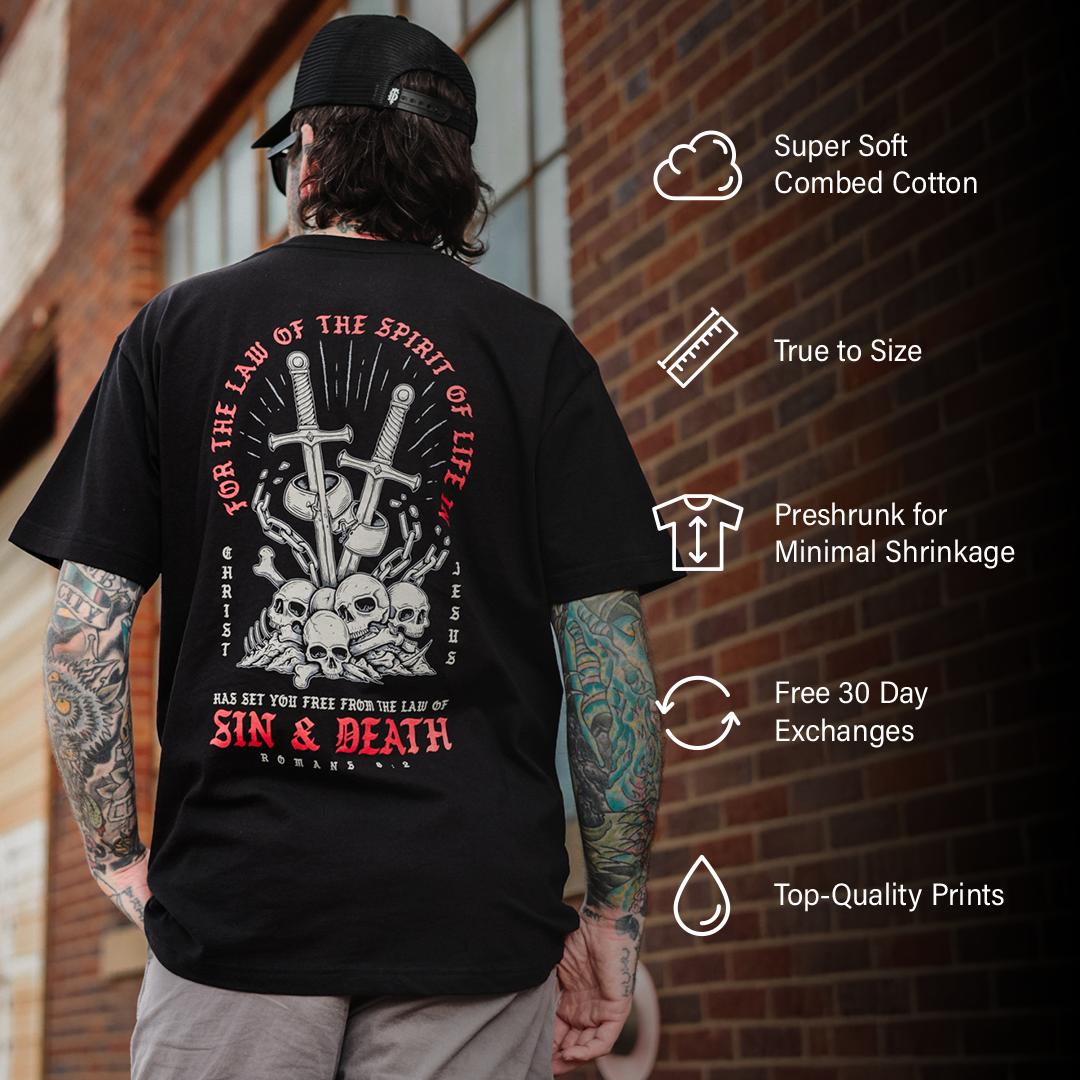 Person wearing a black t-shirt with a graphic design and text, standing against a brick wall.