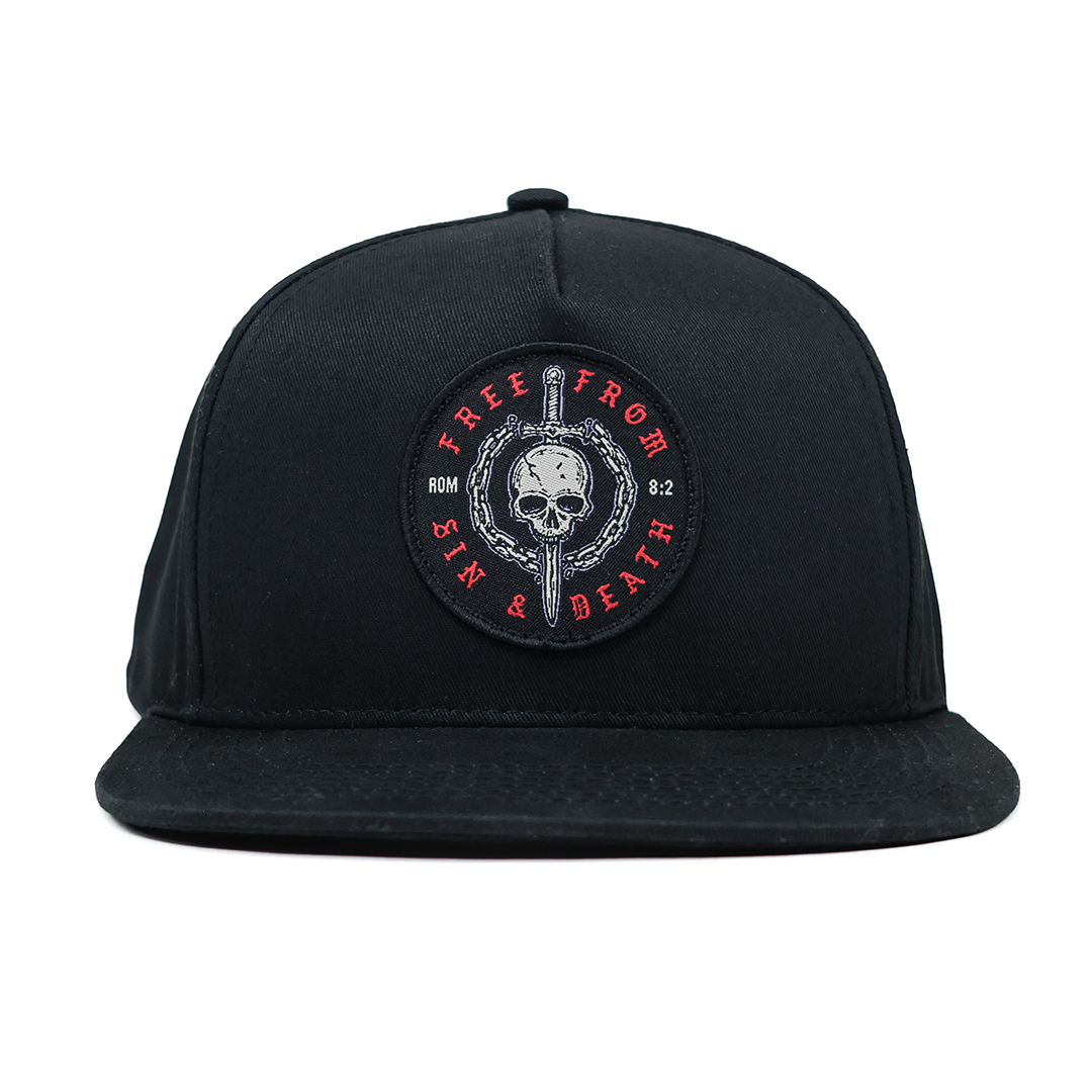 Black Christian cap with a skull and crossbones emblem on a white background. Design inspired by Romans 5:8.