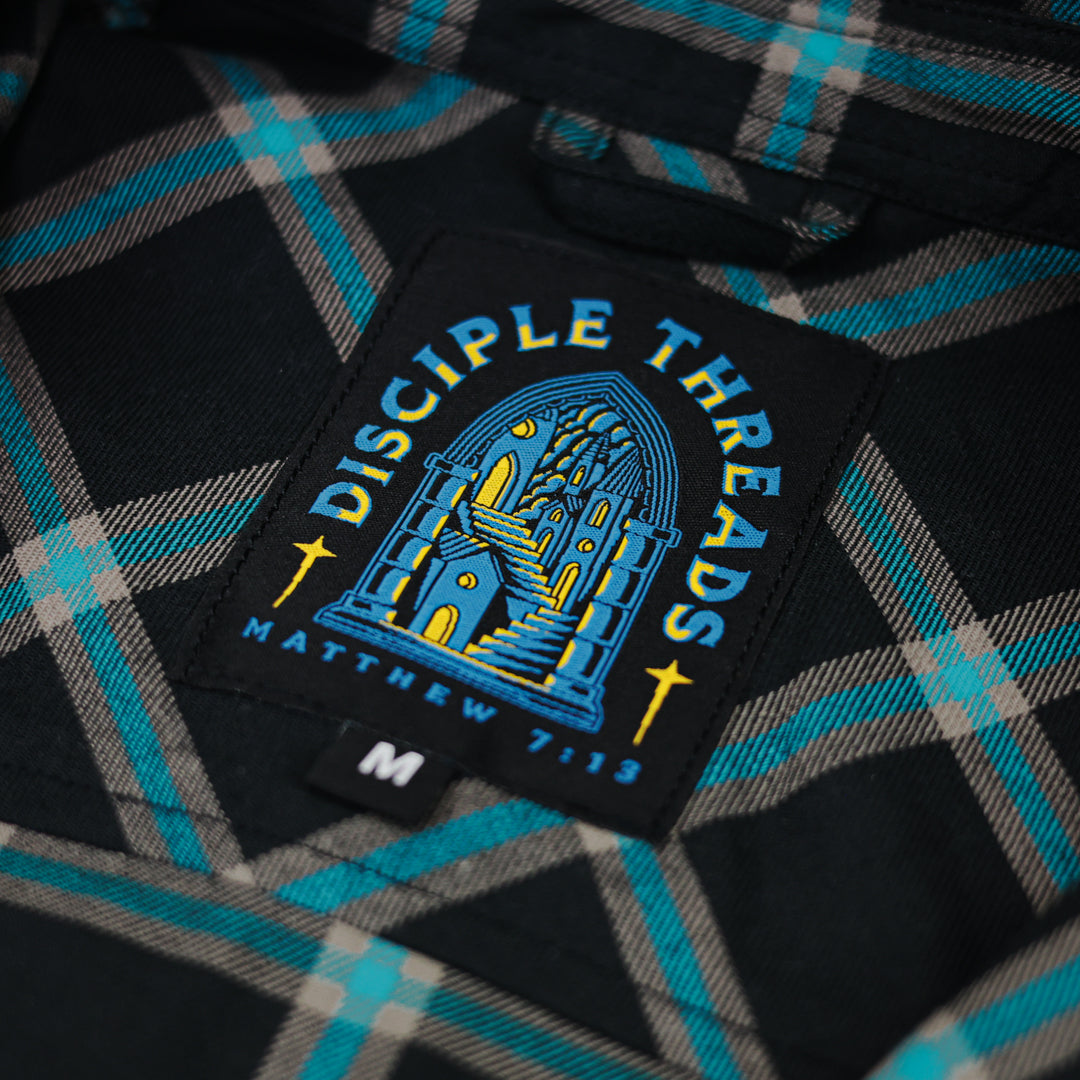 Close-up of a plaid shirt with a 'Disciple Threads' patch featuring Matthew 7:13.