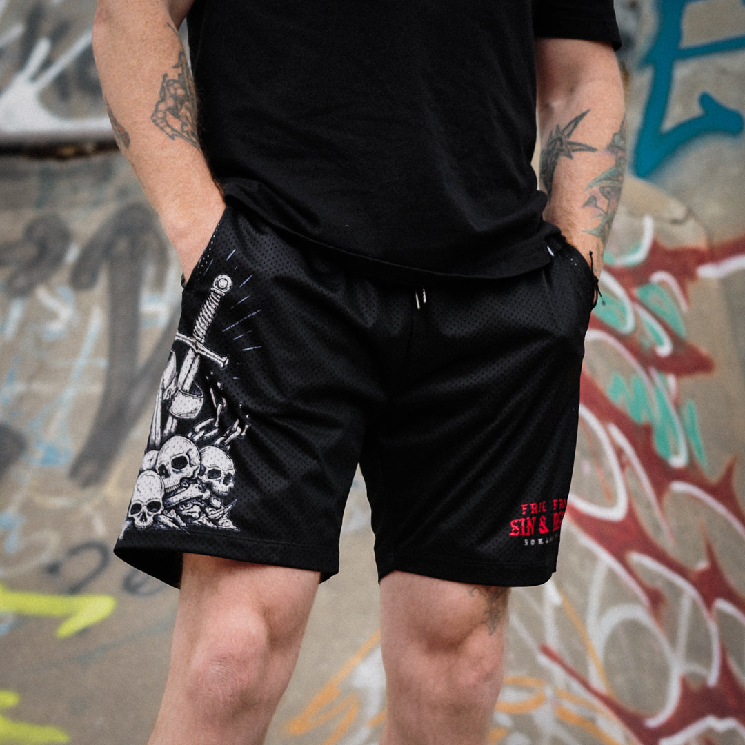 Person wearing black shorts with skull design and text, standing in front of a graffiti-covered wall.
