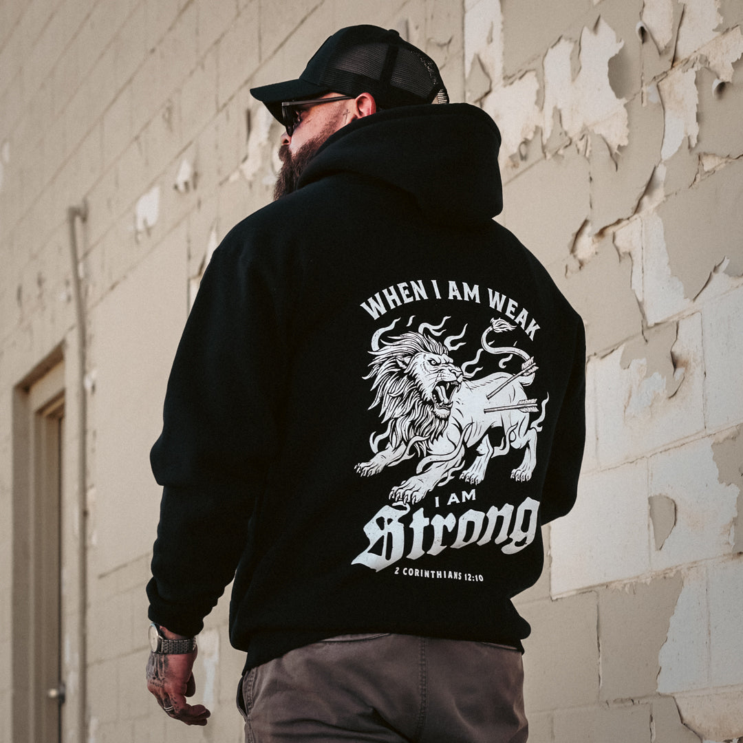 Person wearing a black hoodie with a lion graphic and text against a textured wall.