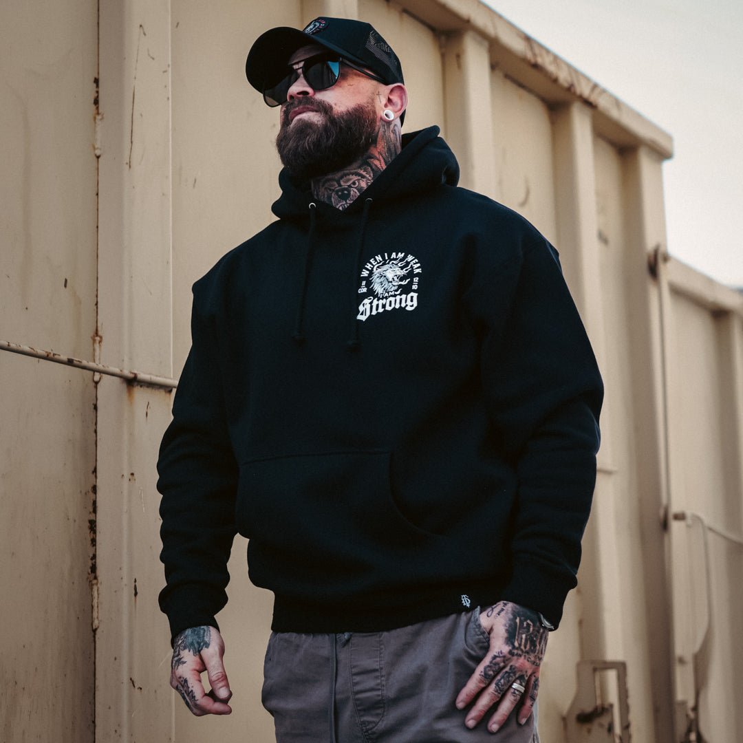 Man wearing a black hoodie with visible branding, standing against a beige wall.