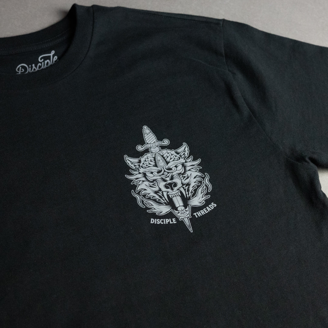 A close-up of a black t-shirt featuring a white graphic print of a wolf head with a dagger and the text 'DISCIPLE THREADS' on the chest. The inner collar shows the brand name 'Disciple' printed in white script.