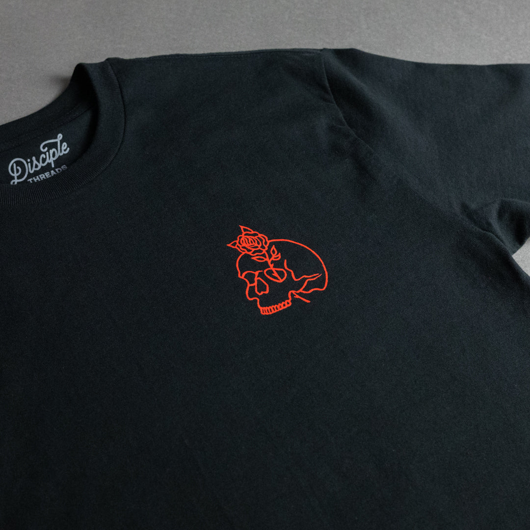 A black crewneck t-shirt featuring a small red line-art graphic of a skull with a rose on the left chest. The inside collar shows the 'Disciple Threads' brand name printed in grey script.
