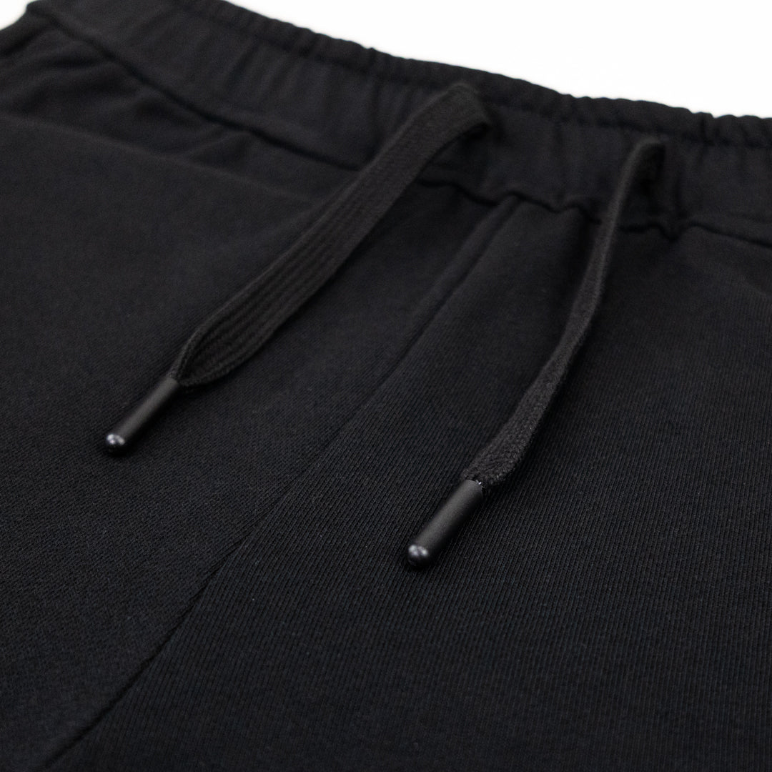 Close-up of black drawstring sweat shorts showing the elastic waistband and black drawstrings with small plastic tips.