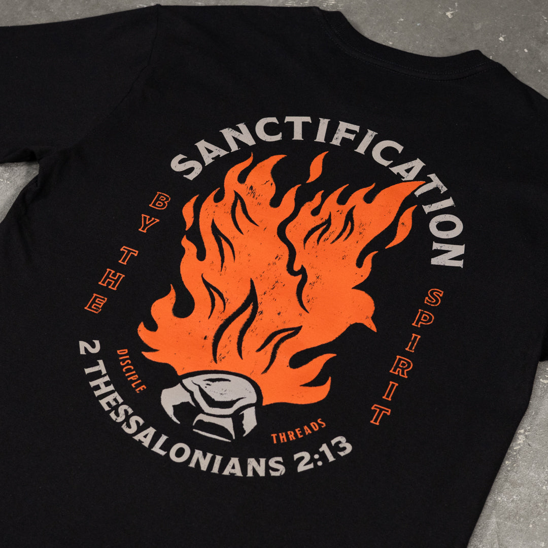 Close-up of the black Sanctification T-shirt graphic, an orange flaming dove rising from a burning coal, framed by Sanctification by the Spirit and 2 Thessalonians 2:13.