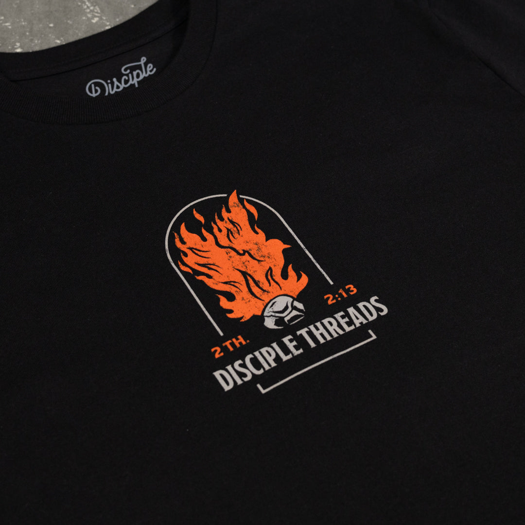 Close-up of the black Sanctification T-shirt chest graphic, an orange flaming dove and coal in an arch above Disciple Threads, 2 Thessalonians 2:13.
