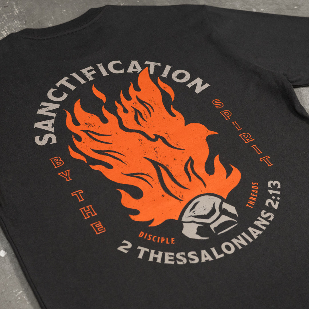 Close-up of the dark grey Sanctification T-shirt graphic, an orange flaming dove rising from a burning coal, framed by Sanctification by the Spirit and 2 Thessalonians 2:13.
