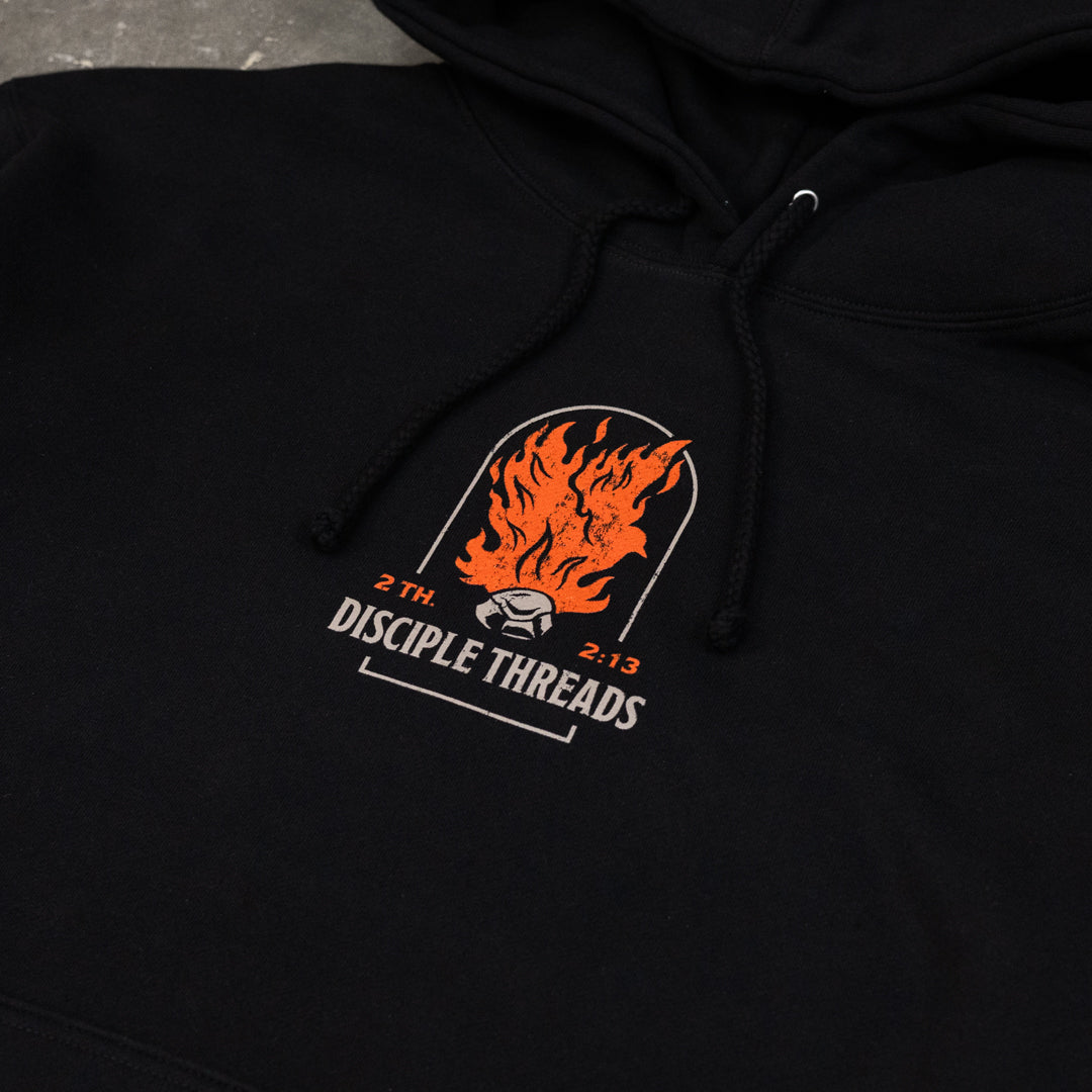 Close-up of the black Sanctification Pullover Hoodie chest graphic, an orange flaming dove and coal in an arch above Disciple Threads, 2 Thessalonians 2:13.