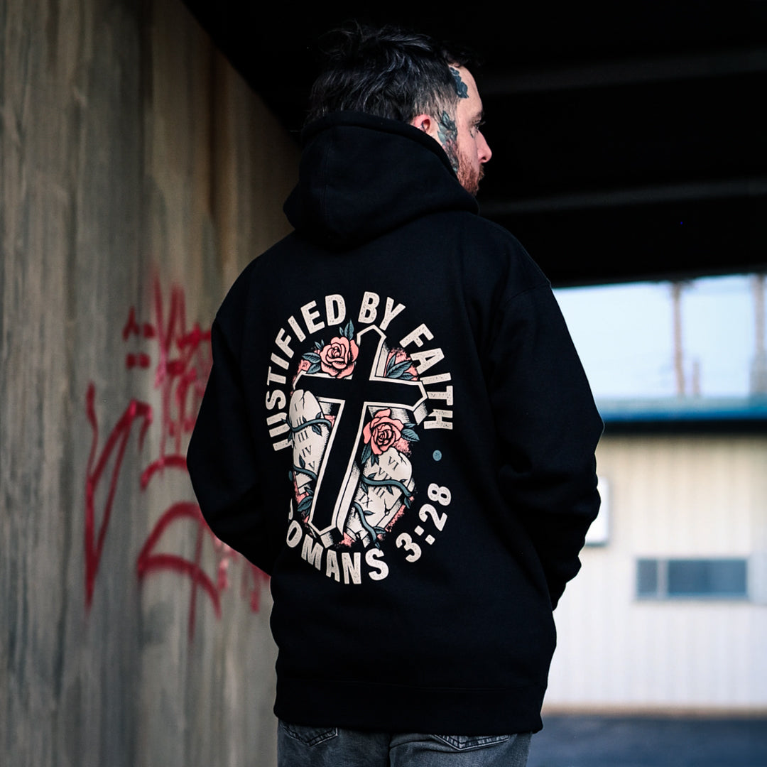 Black Justification zip hoodie with a cream "Justified by Faith, Romans 3:28" graphic: a black cross over the Ten Commandments tablets, wrapped in vines with pink roses.