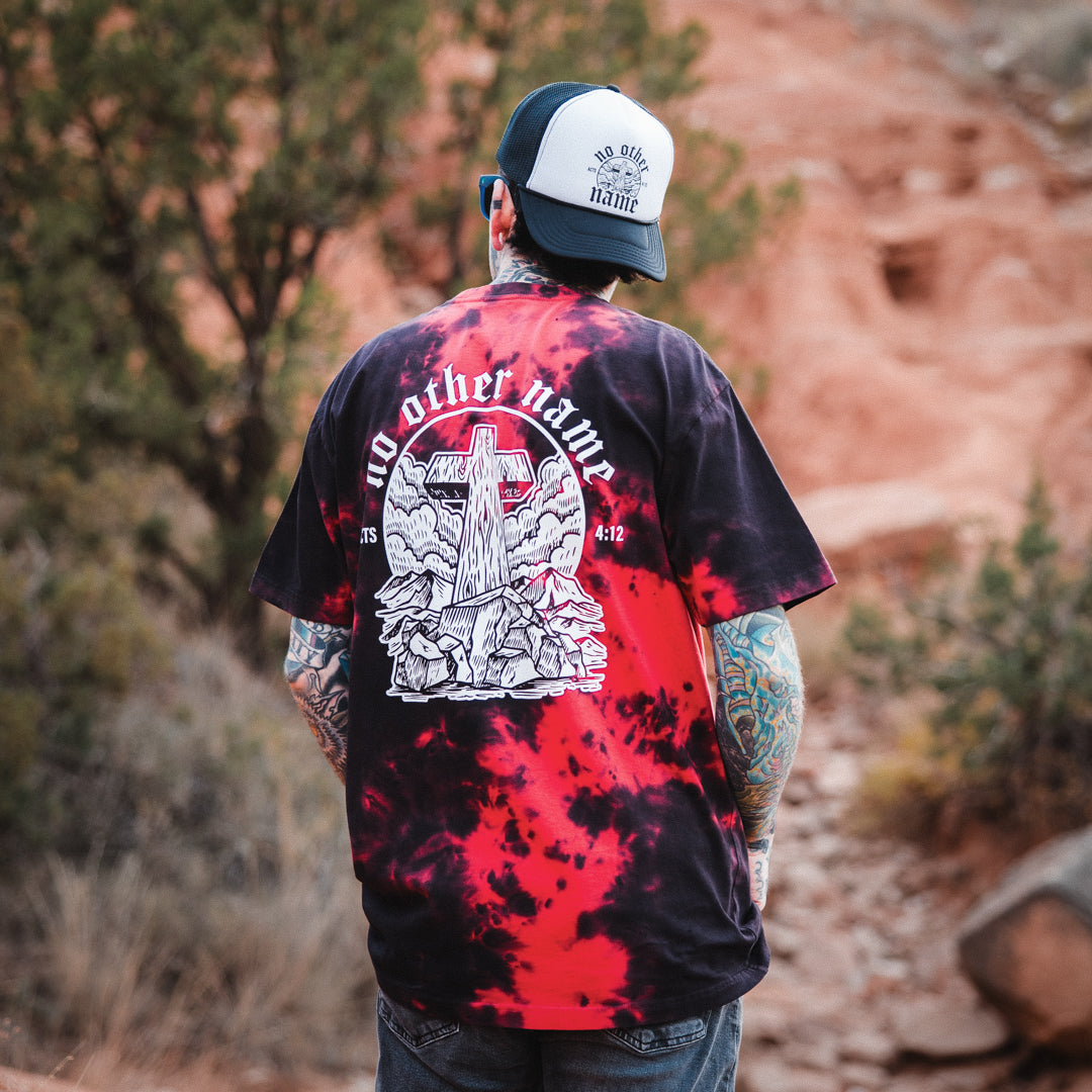Person wearing a tie-dye shirt with a graphic design, standing in a natural setting.