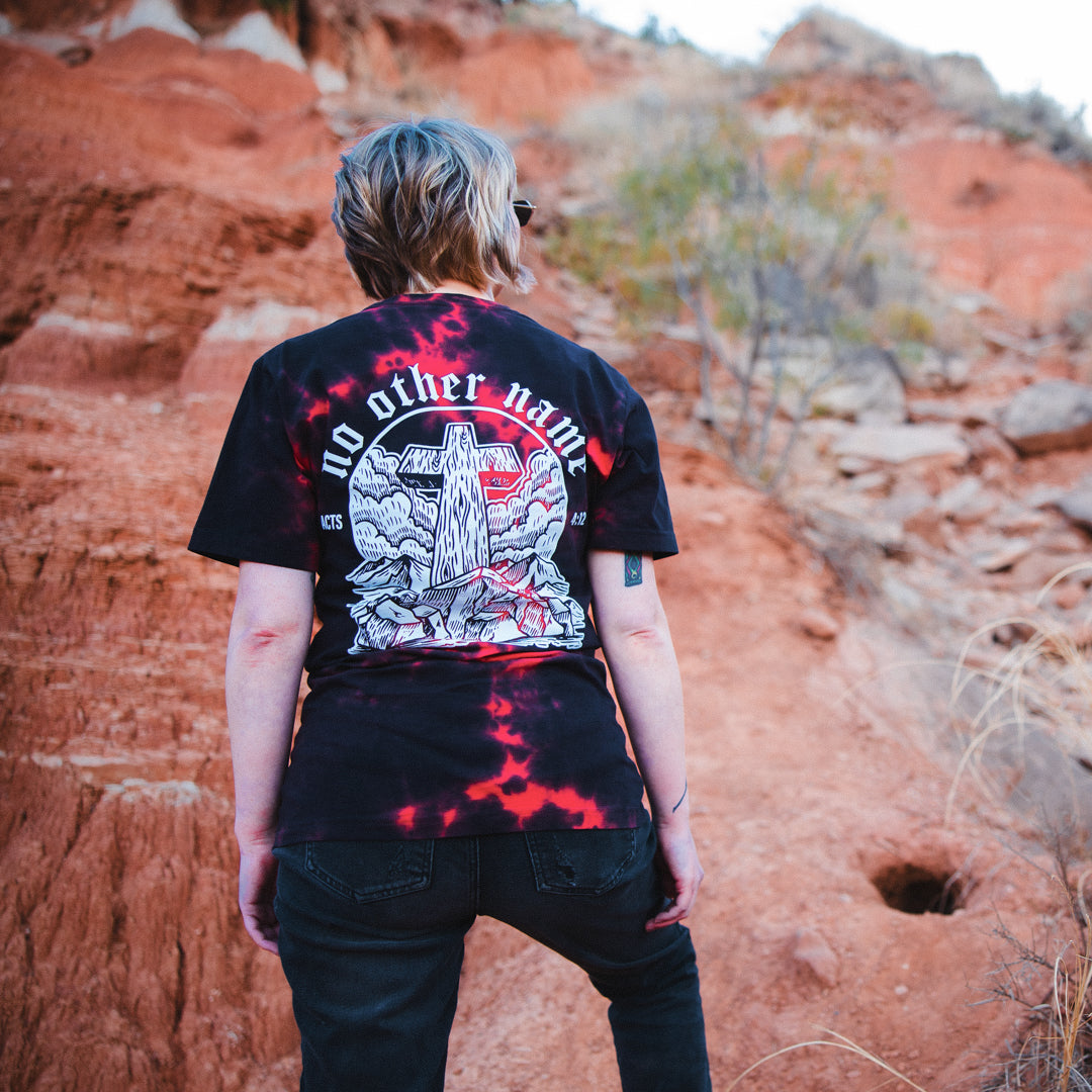 Person wearing a black t-shirt with red and white design in a desert landscape