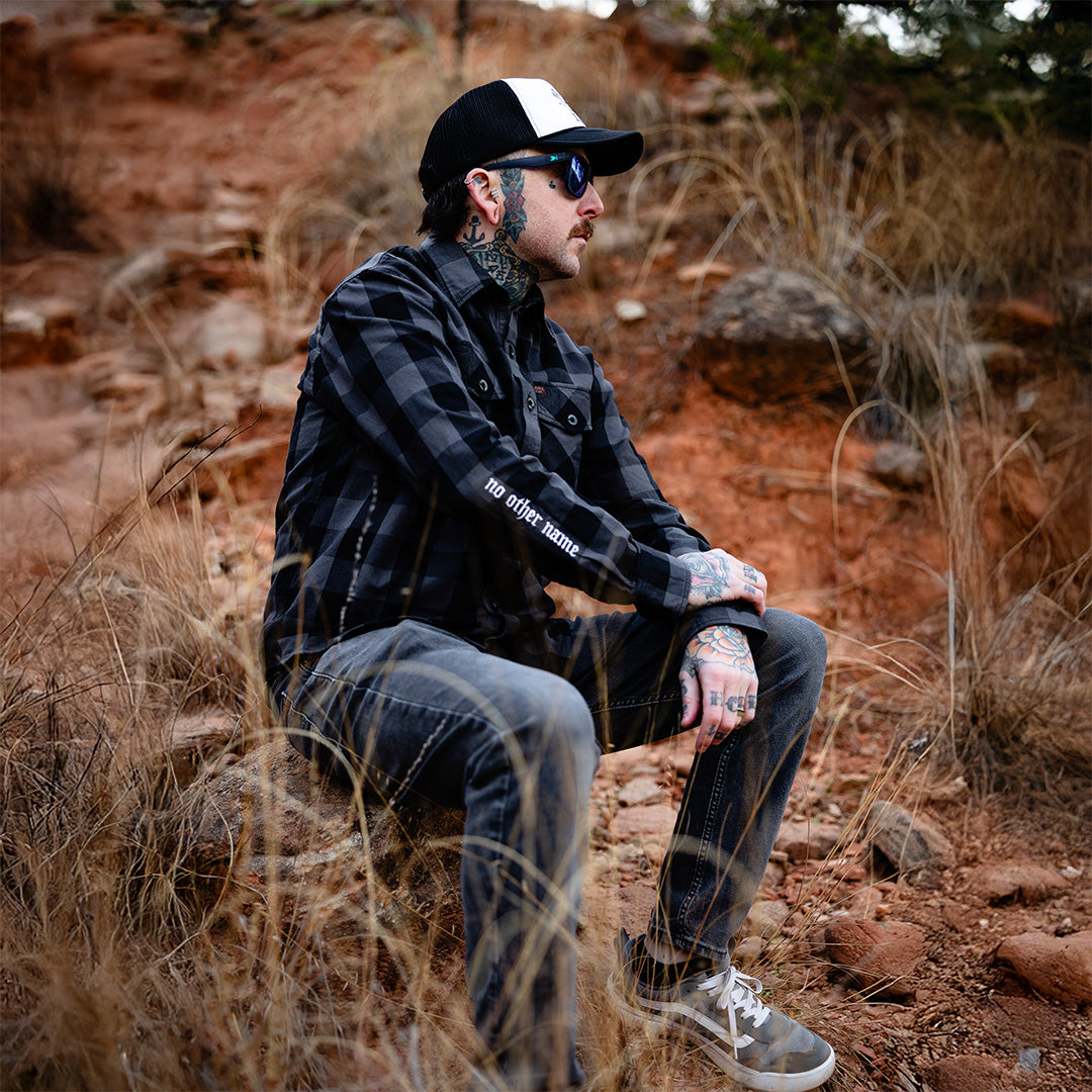 Man sitting on a rocky hillside wearing a flannel and cap.